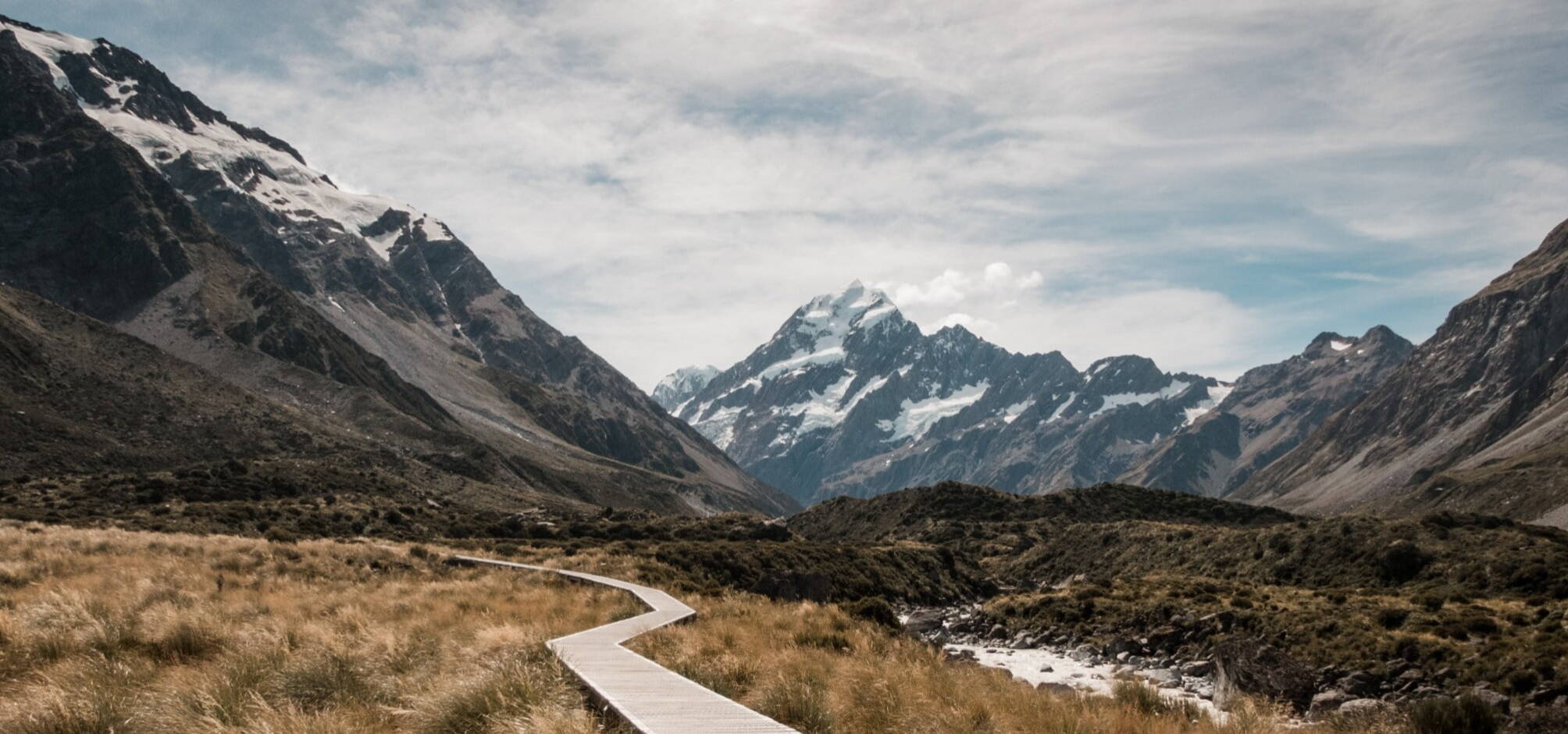 landscape image of a track through low bushland with a snow tipped mountain in the background